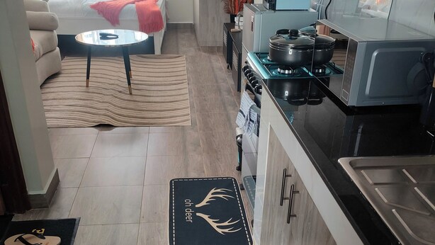 A modern kitchen with a stove, microwave, and sink. There is a dining area with a sofa and a coffee table. - Modern Cosy Studio in Ruaka Near Two Rivers Fast WiFi and fParking,24/7 Security (Nairobi)
