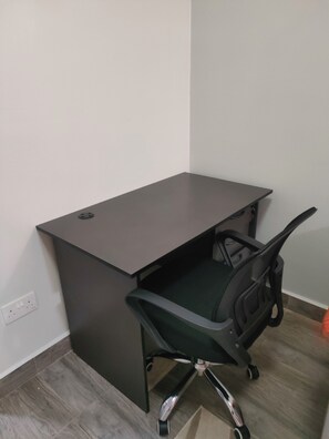 Un bureau avec une chaise, une prise de courant et un coin de pièce dotée d’un plancher en bois.