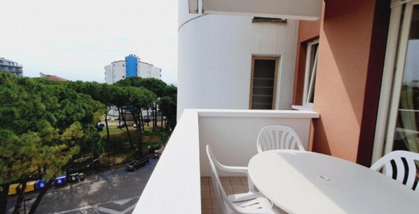 A balcony with a table and chairs, a window, and a view of trees and buildings. - Familiar apartment in a prime location (Lignano Sabbiadoro)