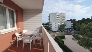 A balcony with white plastic chairs and a table, overlooking a parking area and a multi-story building. - Beachside comfortable retreat (Lignano Sabbiadoro)