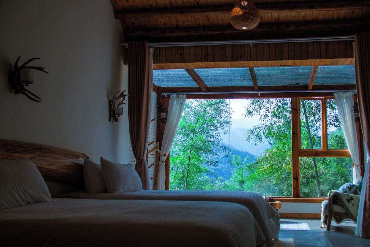 Un dormitorio con un ventanal grande, vigas de madera y una cama con almohadas.
