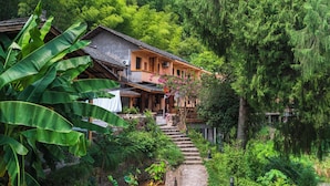 Ein traditionelles Haus mit einer Steintreppe, die zu einem Holzdeck führt, umgeben von üppigem Grün und dichtem Wald.