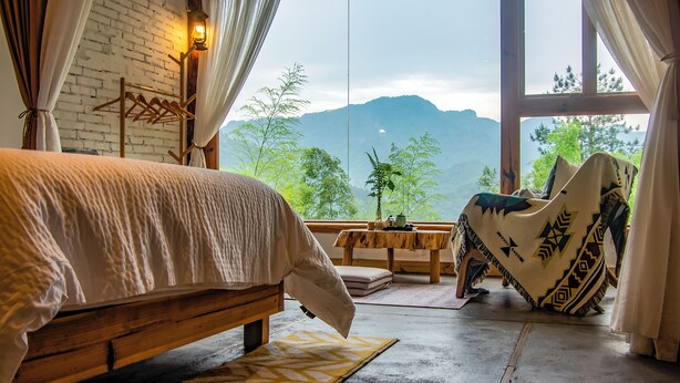 Ein Schlafzimmer mit einem großen Bett, einem Holztisch, einem Stuhl und Bergblick durch ein Fenster.