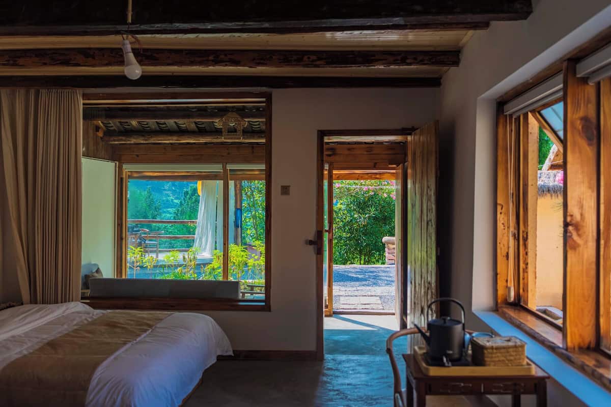 Un dormitorio con cama, ventana, puerta que da al exterior y una mesita con hervidor.