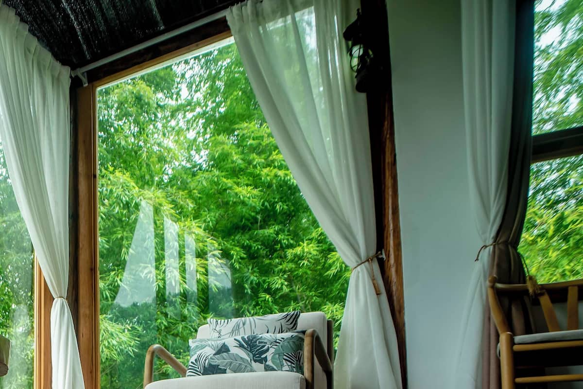 Una habitación con una cama, una silla y vistas a zonas verdes a través de amplios ventanales.