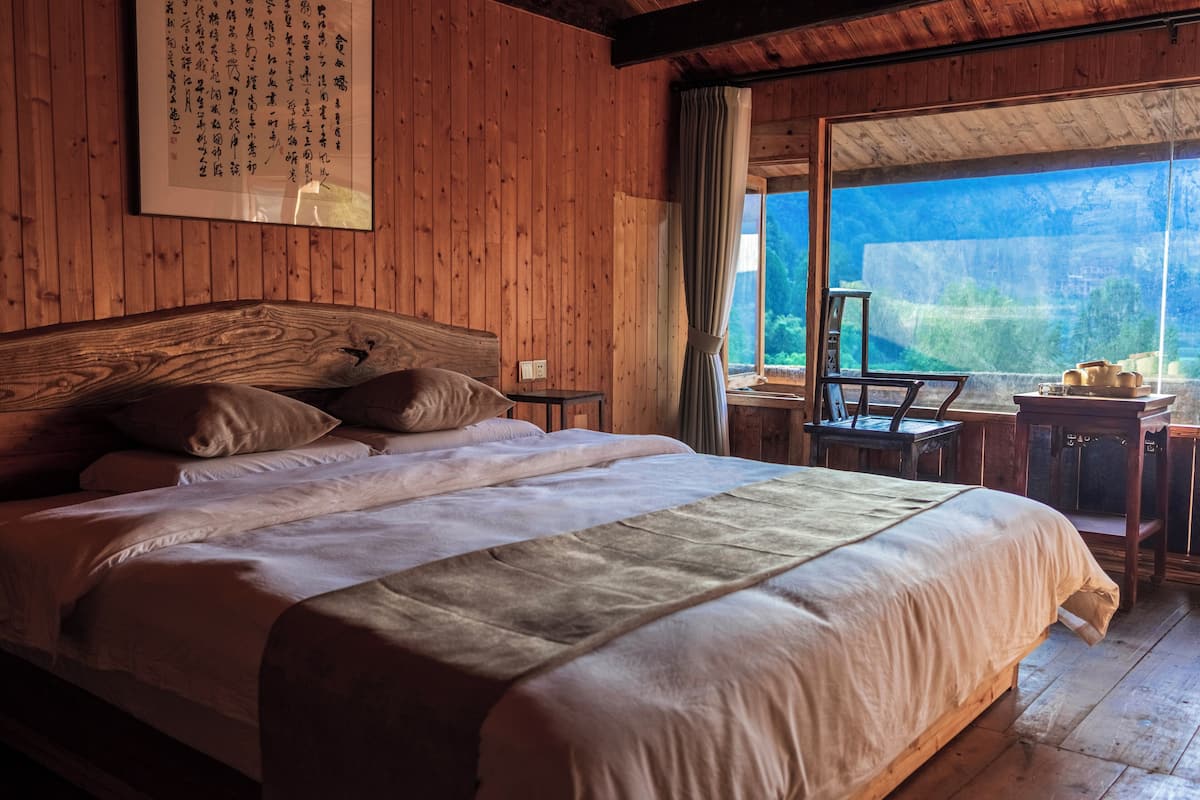 Una habitación de madera con una cama grande, un escritorio y una ventana con vistas a zonas verdes.