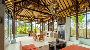 A spacious indoor area with a high ceiling, wooden beams, a dining table with chairs, a sofa, and a kitchen area with a refrigerator. - Suasana Harmonis Private Villa (Ubud)