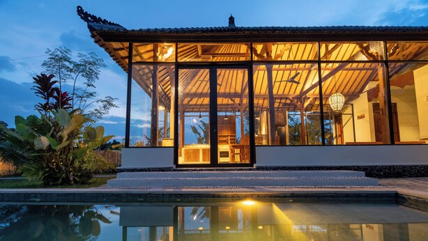 A modern house with a glass facade, a pool in the foreground, and a wooden roof. - Suasana Harmonis Private Villa (Ubud)