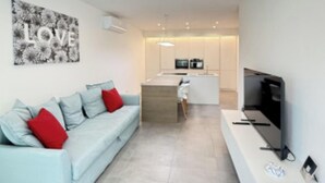Ein modernes Wohnzimmer mit einer Couch, einem Fernseher und einer Küchenzeile im Hintergrund.
