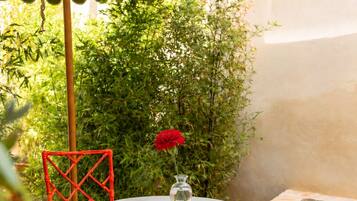 Un patio con una mesa redonda y sillas rojas, un jarrón pequeño con una flor y una piscina al fondo.