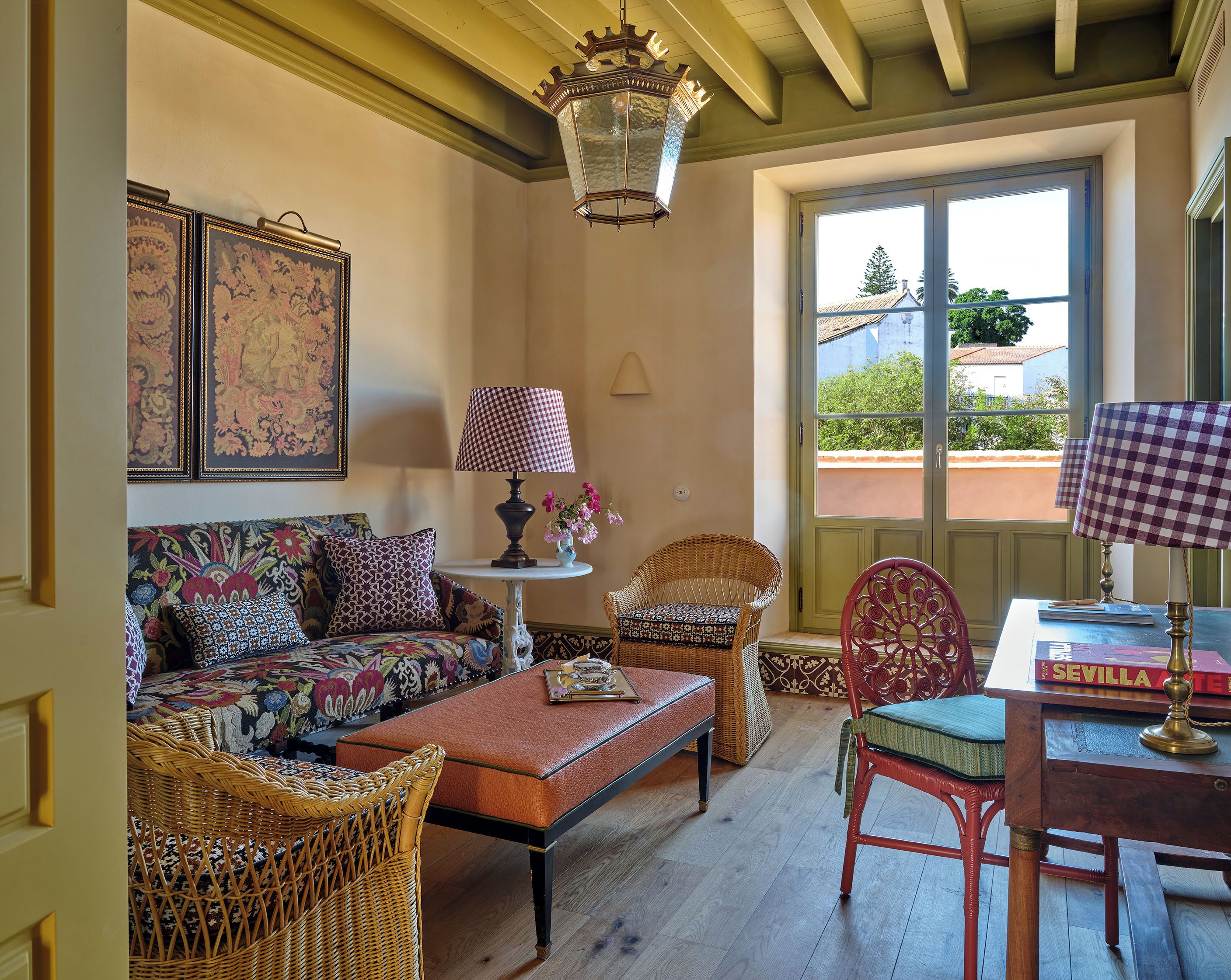 Una sala acogedora con un sofá, dos sillones de mimbre, una mesa con una lámpara y vistas a través de una ventana.