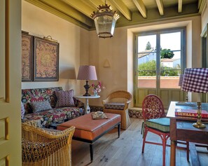 A cozy living room with a sofa, two wicker chairs, a table with a lamp, and a view through a window. - Hotel Casa Góngora - Relais & Châteaux (Villanueva del Ariscal)
