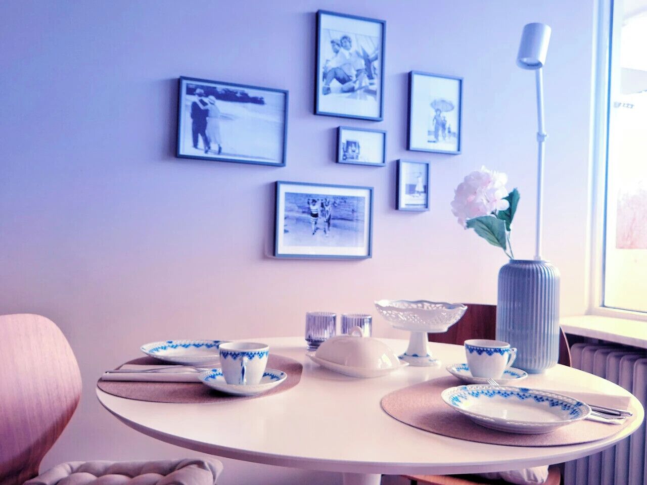 A dining table with plates, cups, and a vase, surrounded by framed pictures on the wall.