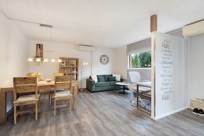 Ein modernes Wohnzimmer mit Essbereich, einem grünen Sofa, einem weißen Sessel und einer Wanduhr.