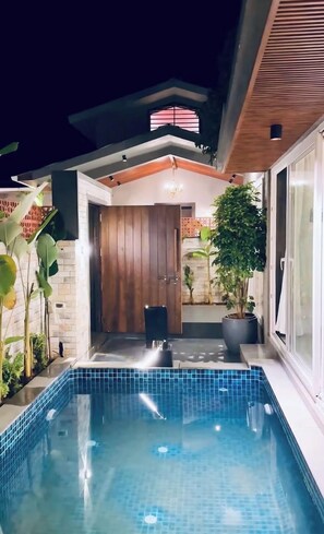 Uma área de piscina moderna ao ar livre, com porta de madeira, plantas em vasos e piscina revestida em azulejo.