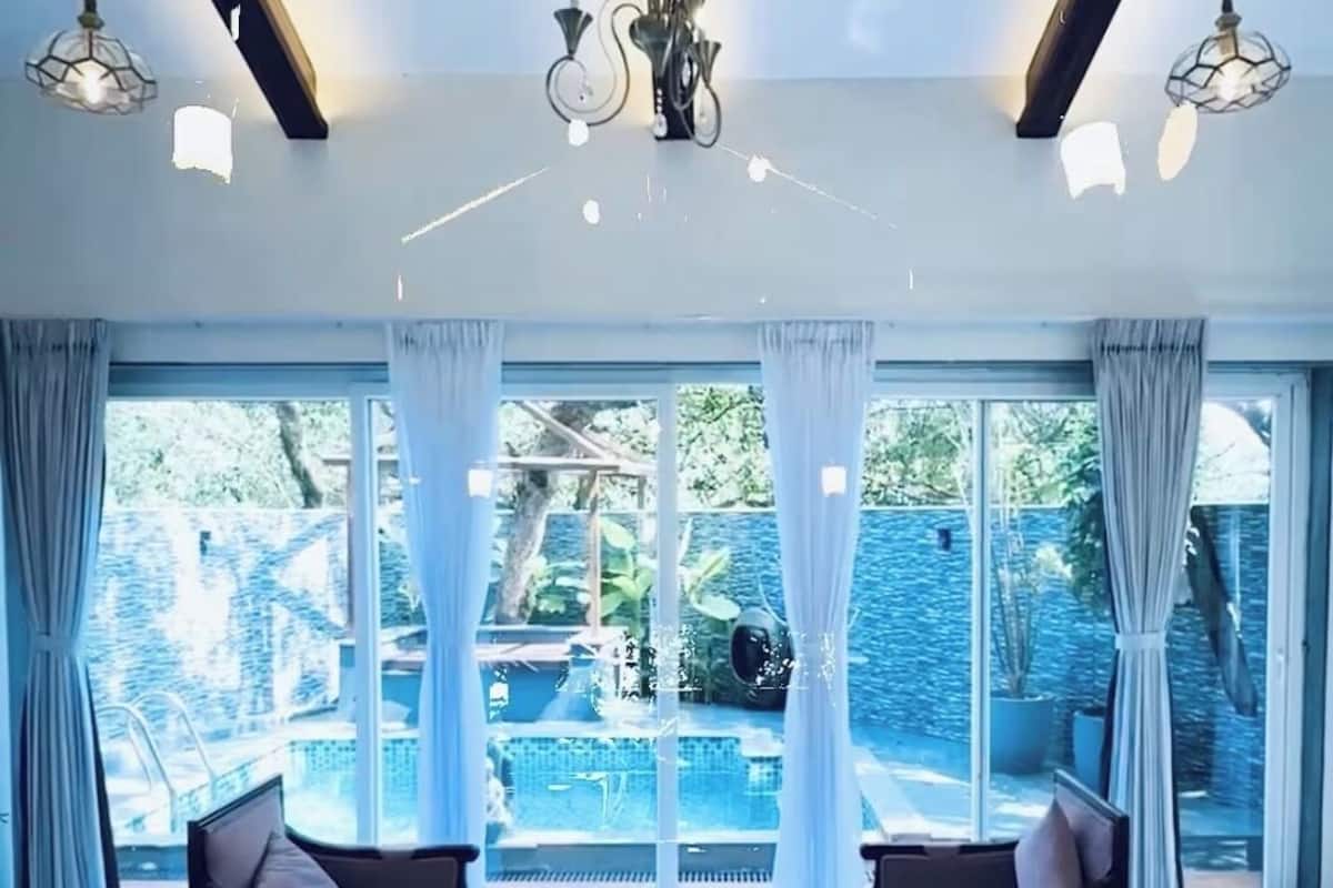 En rummelig stue med en stor sofa, et sofabord i glas og udsigt til en swimmingpool og grønne områder.