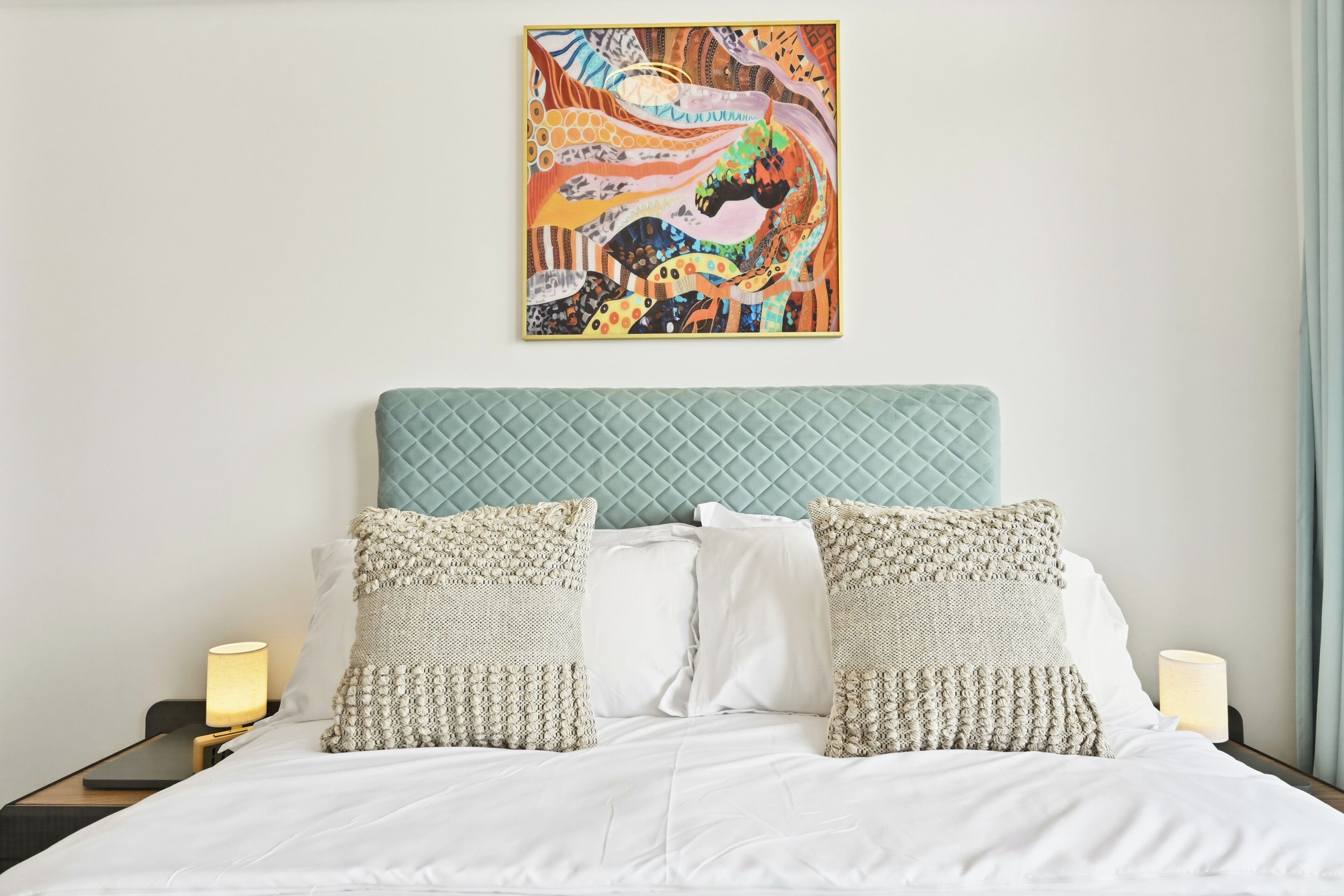 A bed with white bedding, quilted headboard, and decorative pillows.