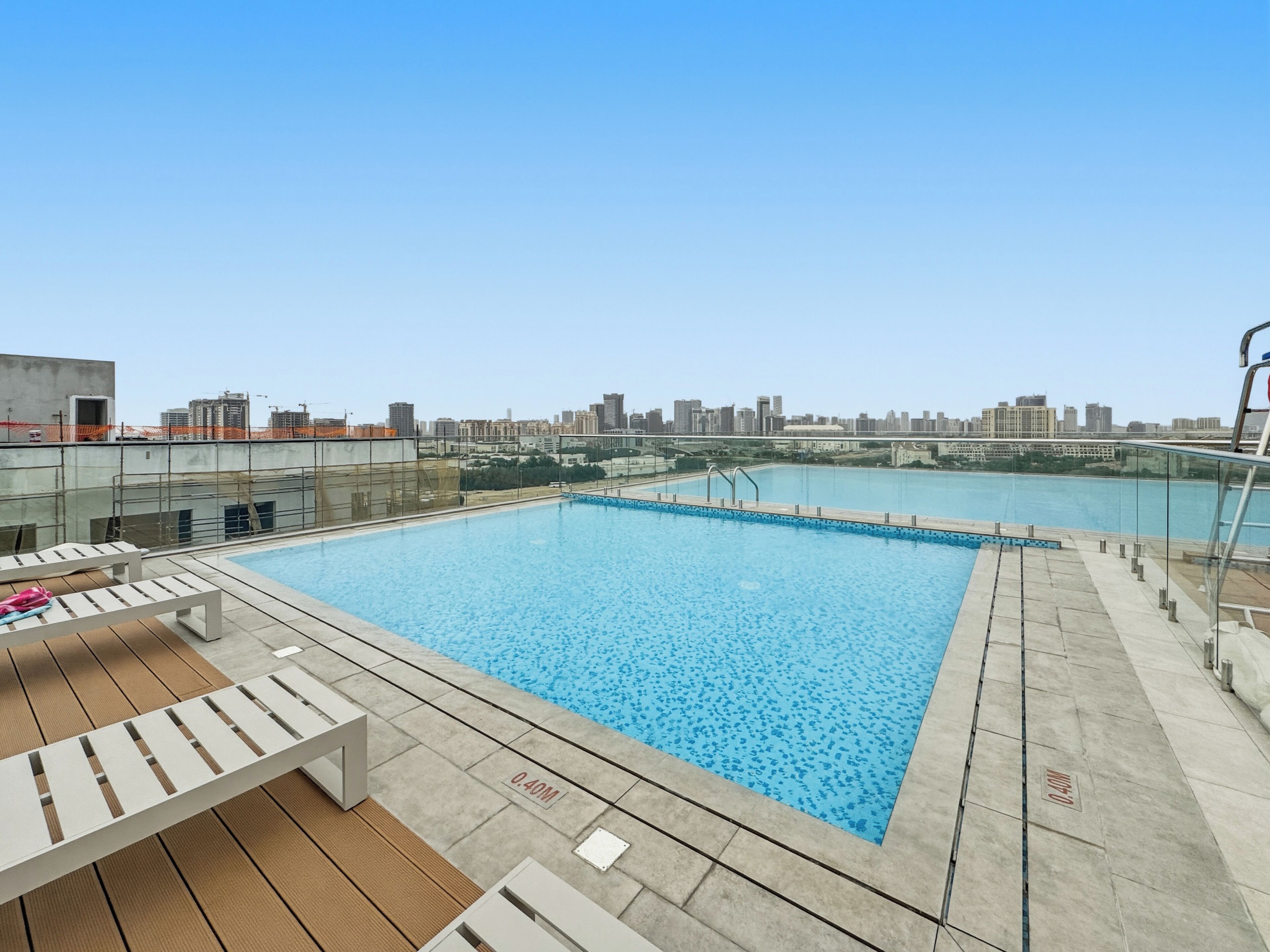 A rooftop pool with a city view, lounge chairs, and a clear sky.