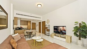 A modern living room with a sofa, TV, dining area, and kitchen in the background. - Bloomfields Modern 1BR in Azizi Vista (Dubai)