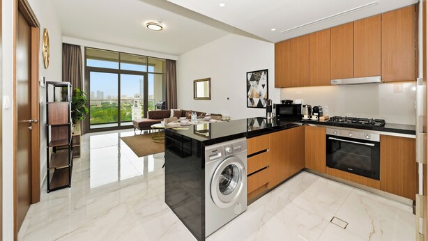 A modern kitchen with a built-in washer, a dining area with a view, and wooden cabinets. - Bloomfields Modern 1BR in Azizi Vista (Dubai)