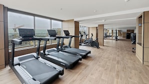 A modern gym with treadmills, exercise bikes, and a view of a construction site. - Bloomfields Modern 1BR in Azizi Vista (Dubai)