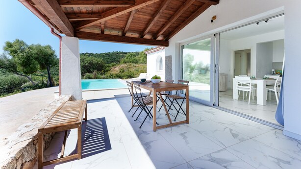 Un patio techado al aire libre con una mesa y sillas de madera, una piscina y vistas a una colina.