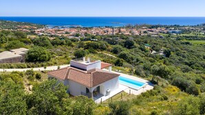 Una villa moderna con piscina, rodeada de vegetación exuberante y con vistas a un pueblo costero.