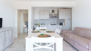 Una cocina moderna con armarios blancos, una mesa de comedor con sillas y un sofá en un espacio luminoso y bien iluminado.