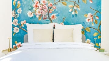 Une chambre à coucher avec un lit, des oreillers, une table de chevet et un mur orné d’un tableau représentant des motifs floraux.