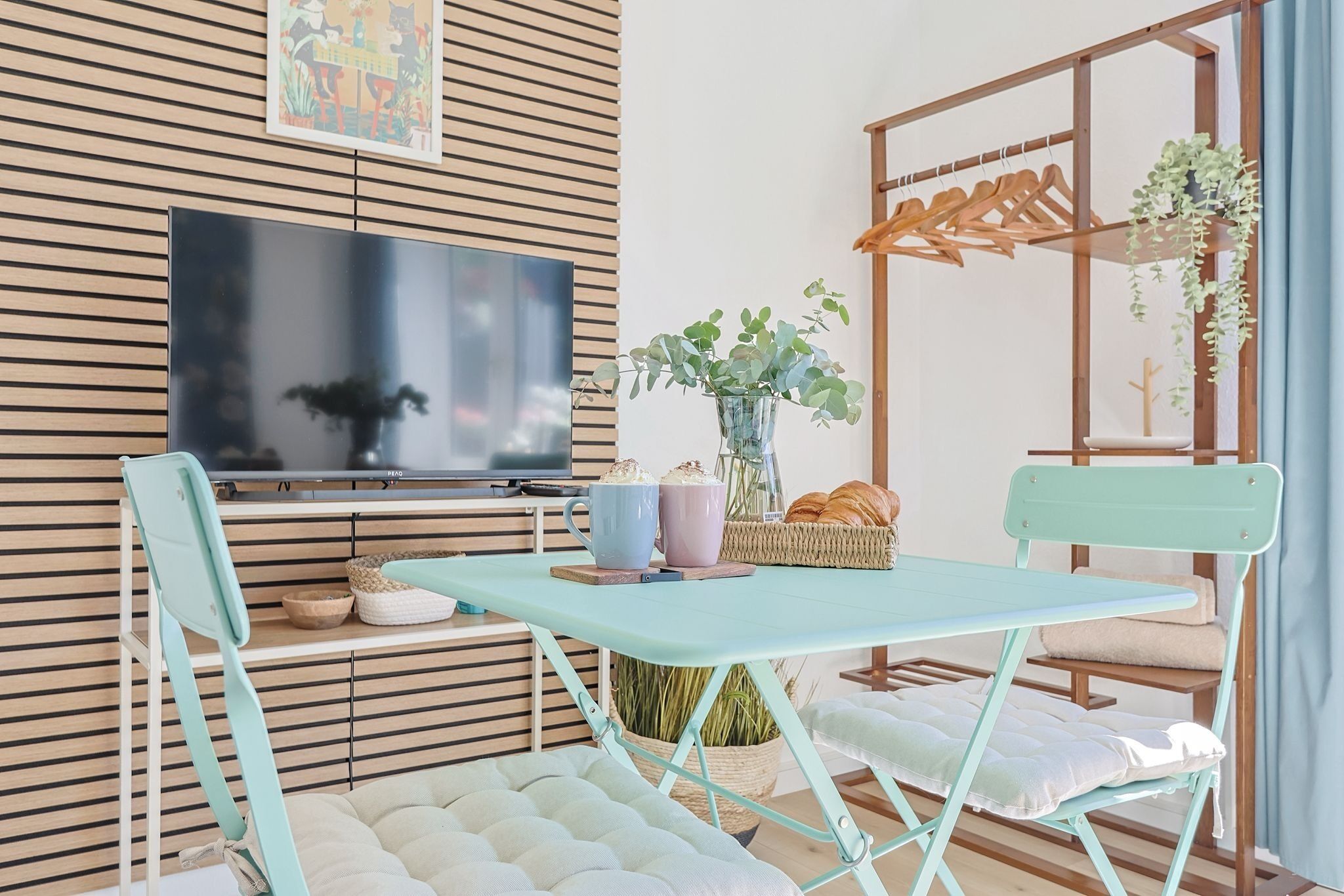 Een kamer met een opklapbare tafel, twee stoelen, een televisie, een plant en een houten wandpaneel.