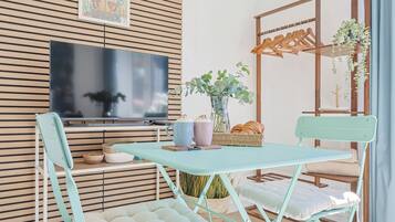 Een kamer met een opklapbare tafel, twee stoelen, een televisie, een plant en een houten wandpaneel.