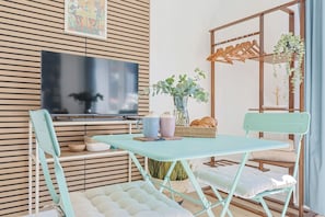 Een kamer met een opklapbare tafel, twee stoelen, een televisie, een plant en een houten wandpaneel.