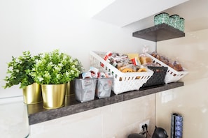 En køkkenhylde med krukkeplanter, kurve med dagligvarer og en kaffemaskine.