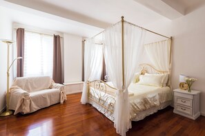 Ein Himmelbett mit Baldachin, ein Nachttisch mit Lampe und ein abgedecktes Sofa.