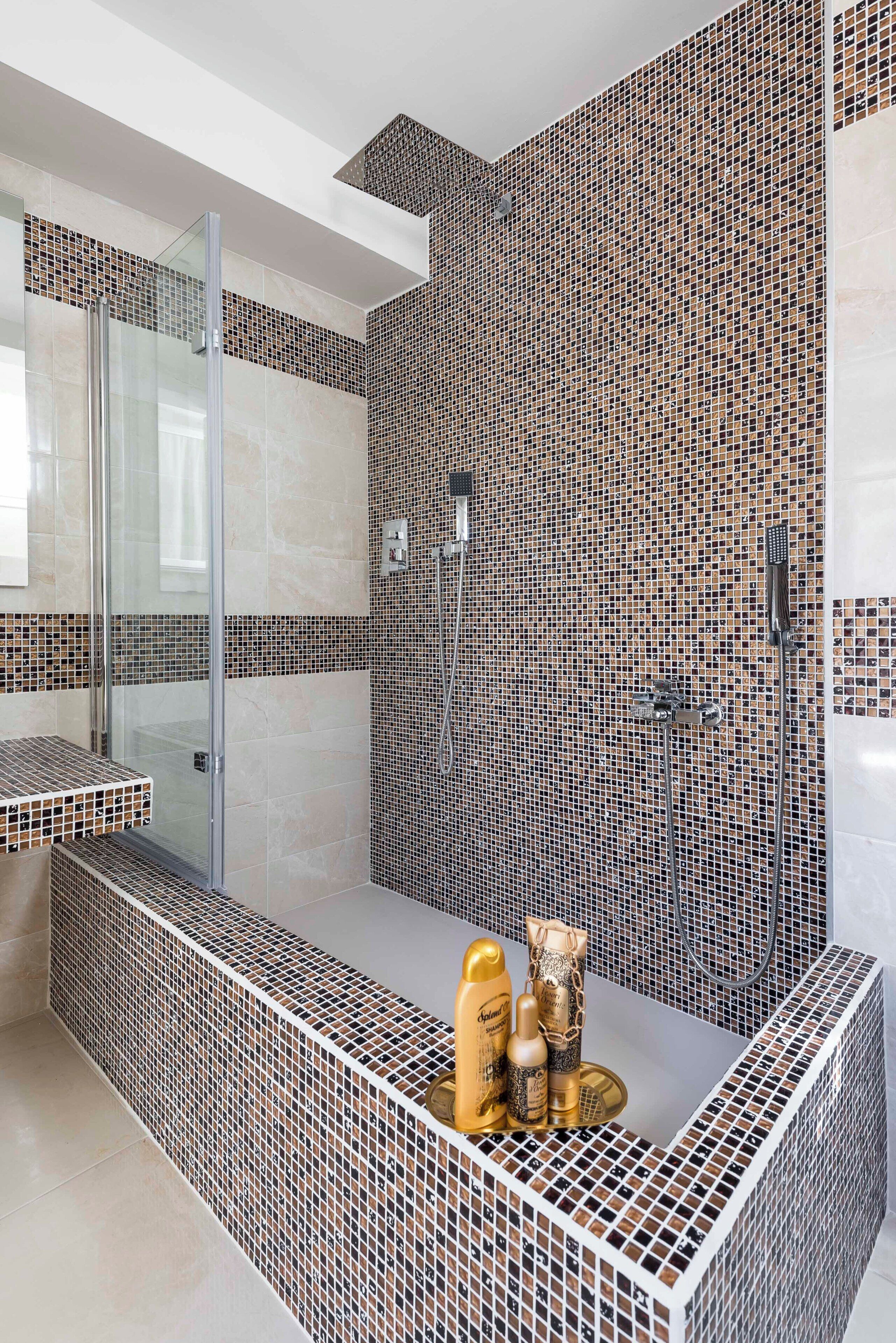A modern bathroom with mosaic tile walls, a glass shower enclosure, and a vanity with toiletries.