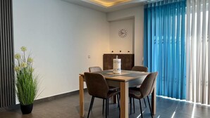 A modern dining area with a wooden table, four chairs, a potted plant, and a clock on the wall. - Luzzu Harbour Suites Modern 2BR in Marsaxlokk (Marsaxlokk)