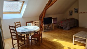 Ein Zimmer mit schrägem Dach, einem runden Tisch mit Stühlen, einem Bett, einem Fernseher und einem Fenster.