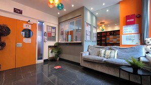 A reception area with a sofa, a plant, a fire safety notice, and a control panel.