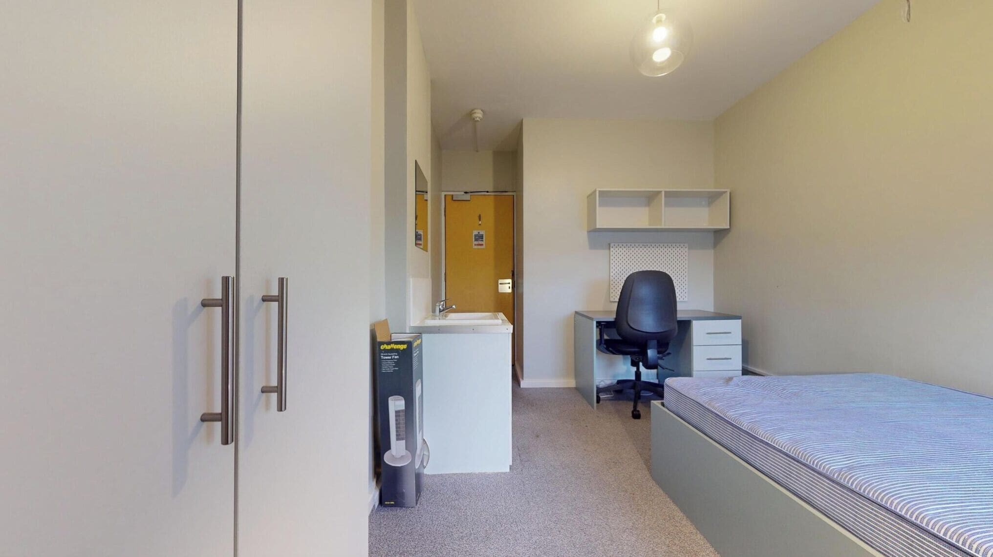 Een compacte, praktische slaapkamer met een bed, bureau, stoel en kledingkast.