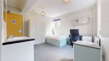 A modern bedroom with a bed, a desk, a chair, and a bathroom with a sink and mirror.