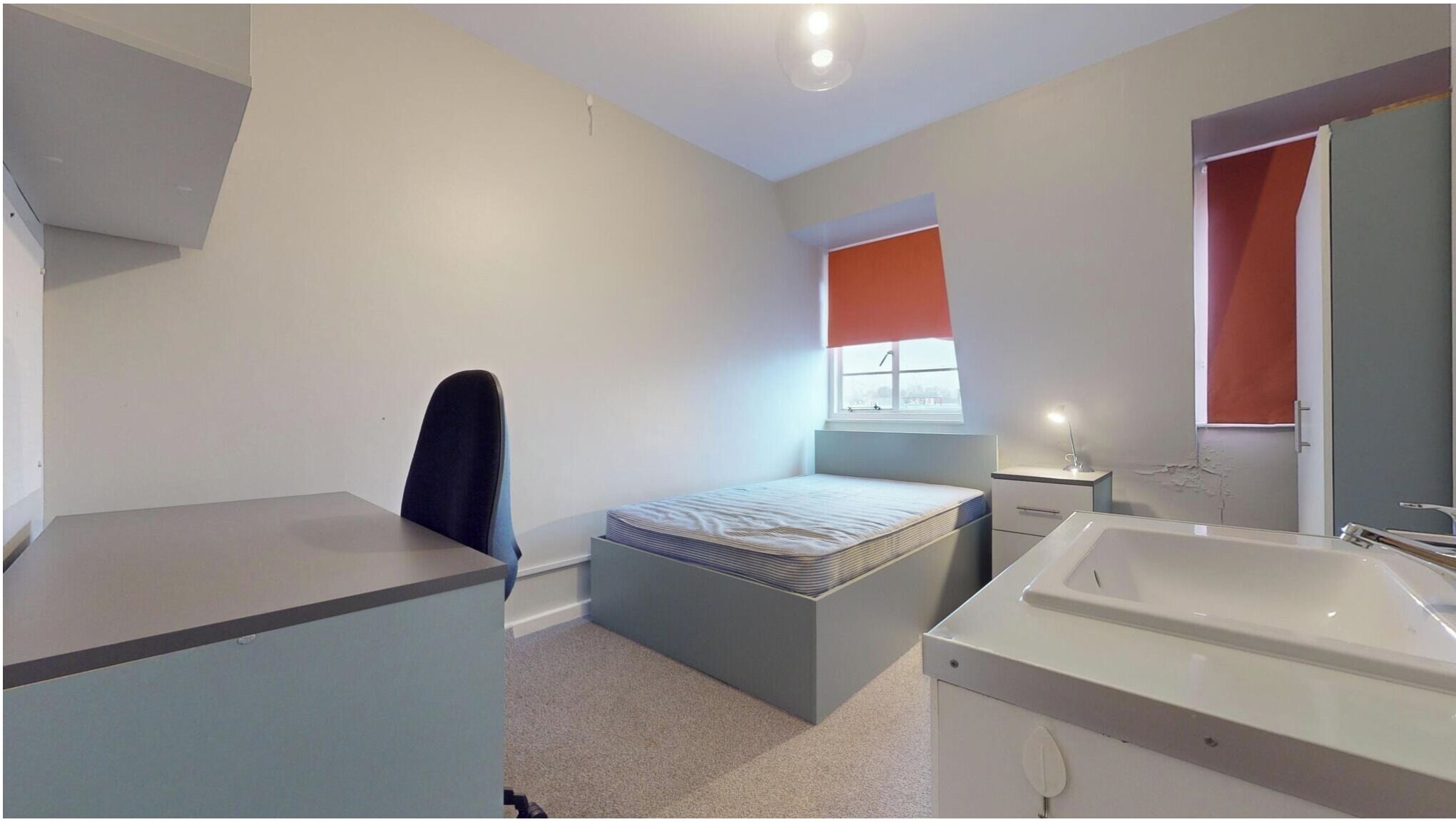 Une chambre à coucher comprenant un lit, un bureau, une chaise, une table de chevet, un miroir, ainsi qu’une salle de bain avec un lavabo et une baignoire.