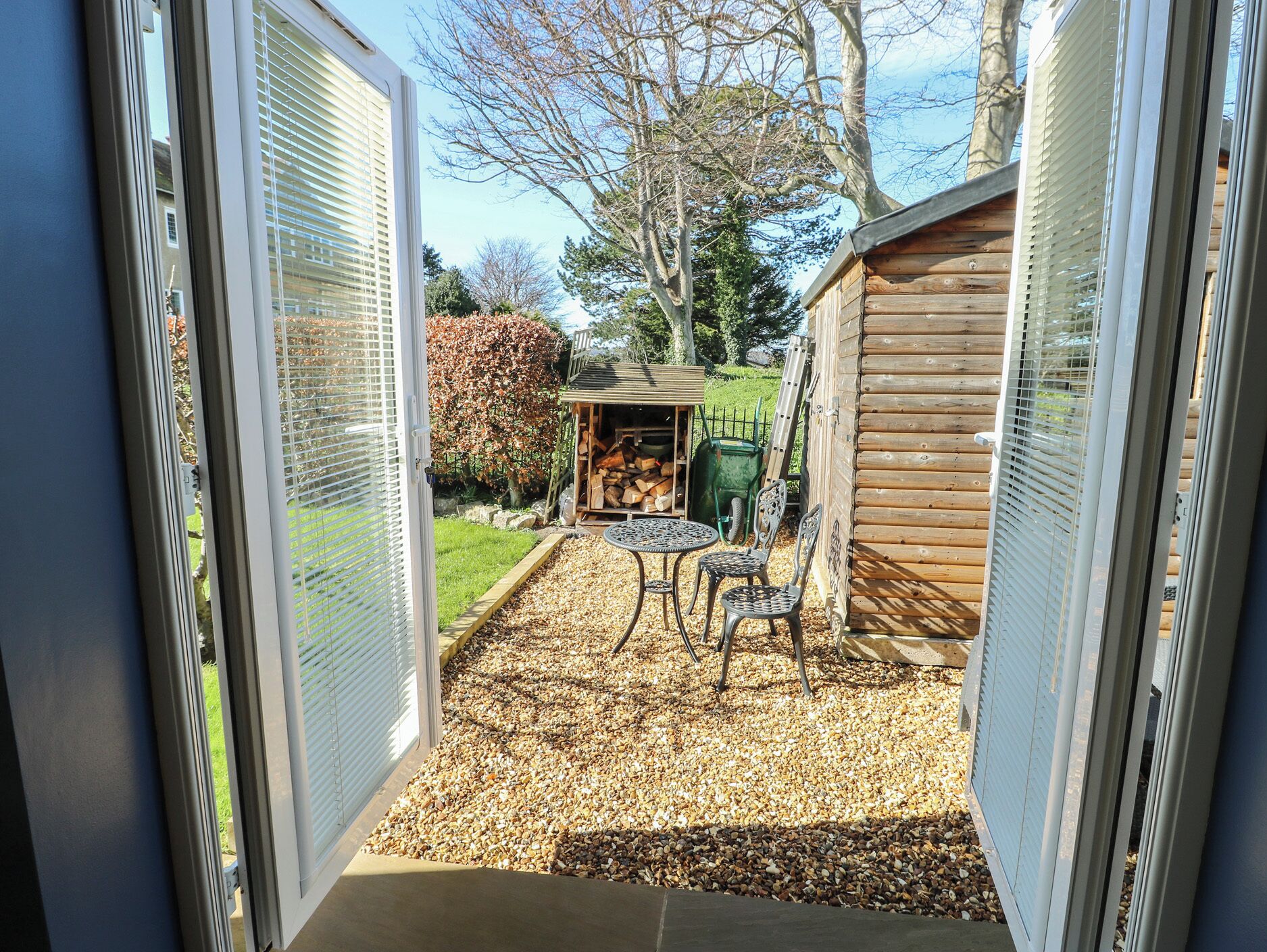 Une terrasse avec une table et des chaises, un abri de jardin et un jardin avec des arbres et une pelouse.