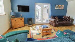 A living room with a sofa, a coffee table, a television, a fireplace, and a sliding glass door. - Trillo Lodge (Colwyn Bay)