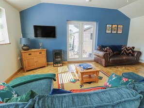 A living room with a sofa, a coffee table, a television, a fireplace, and a sliding glass door. - Trillo Lodge (Colwyn Bay)