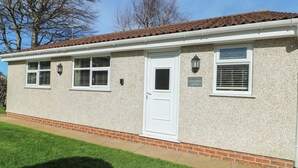 A single-story building with a white door, two windows with shutters, and a small porch area. - Trillo Lodge (Colwyn Bay)