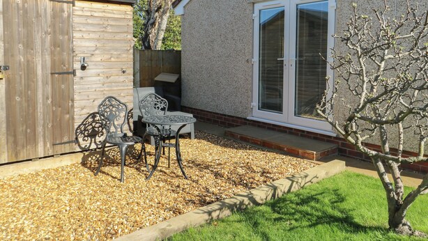 A patio with a table and chairs, a wooden shed, and a house with a sliding glass door. - Trillo Lodge (Colwyn Bay)