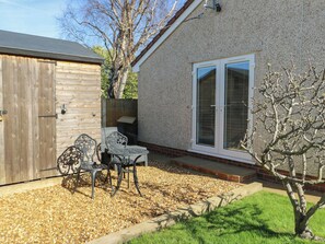 A patio with a table and chairs, a wooden shed, and a house with a sliding glass door. - Trillo Lodge (Colwyn Bay)