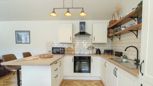 A modern kitchen with white cabinets, a wooden countertop, a built-in oven, a microwave, a coffee machine, and a hanging light fixture. - Trillo Lodge (Colwyn Bay)