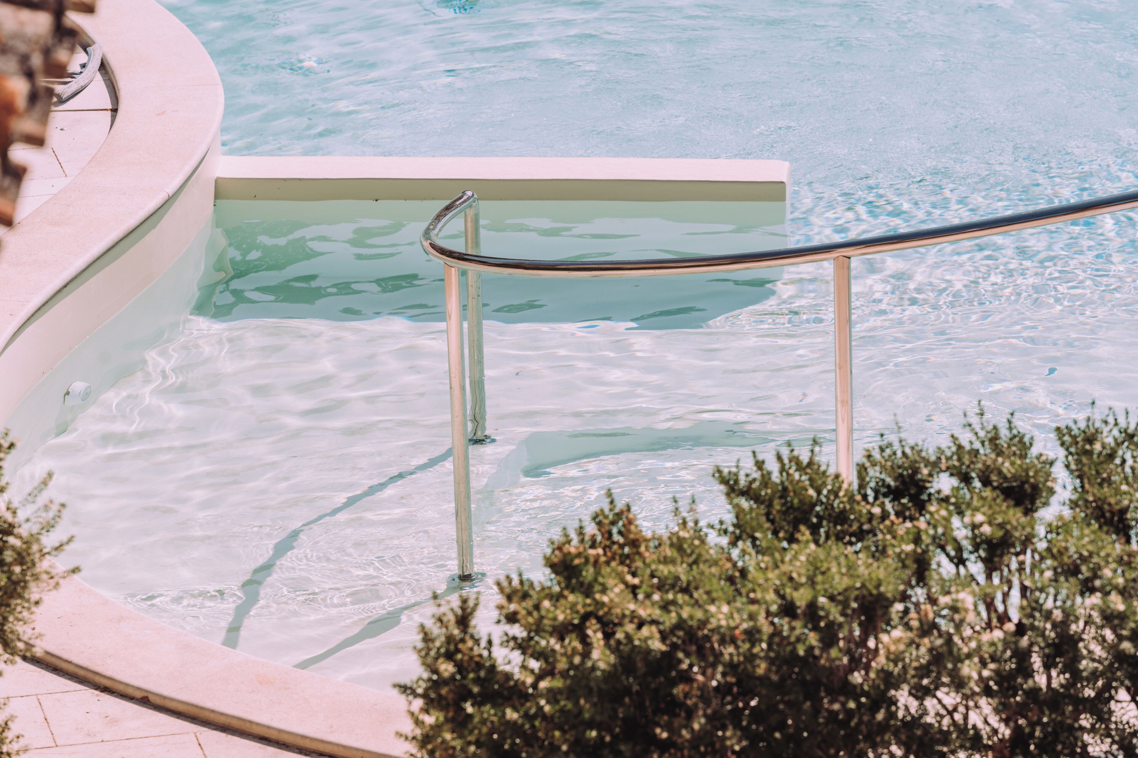 Ein Pool mit klarem Wasser, einem Metallgeländer und einer gefliesten Kante.