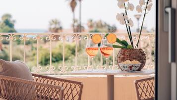 Ein Balkon mit Korbstühlen, einem Tisch mit zwei Gläsern rotem Getränk, einem Korb voller Blumen und einer Schüssel mit Snacks.